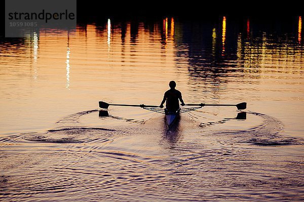 Junger Mann rudert bei Sonnenuntergang auf dem Fluss.