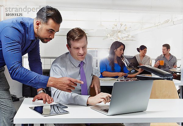 Zwei Geschäftsleute im Gespräch  Blick auf den Laptop  Kollegen im Hintergrund