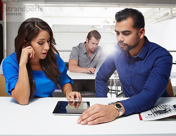 Geschäftsfrau und Geschäftsmann am Schreibtisch sitzend  mit Blick auf das digitale Tablett