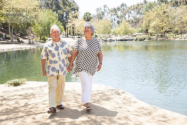Seniorenpaar geht Hand in Hand am See entlang