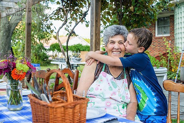 Junge umarmt und küsst Großmutters Wange beim Tomatenfest