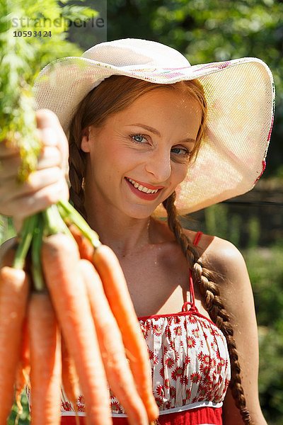 Porträt einer mittleren erwachsenen Frau im Garten  die einen Haufen Karotten hält.