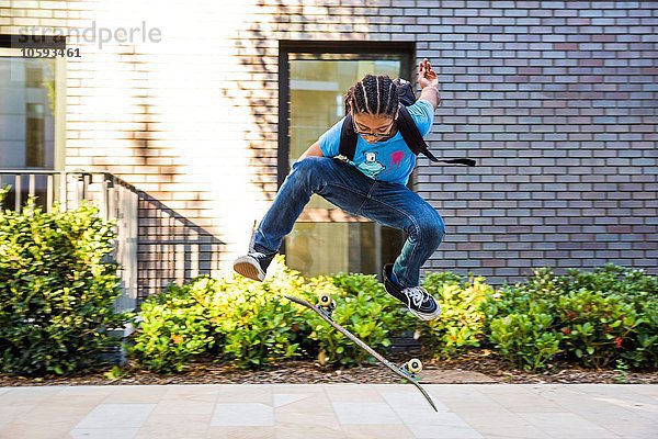 Junge macht Skateboard-Tricksprung auf städtischem Bürgersteig