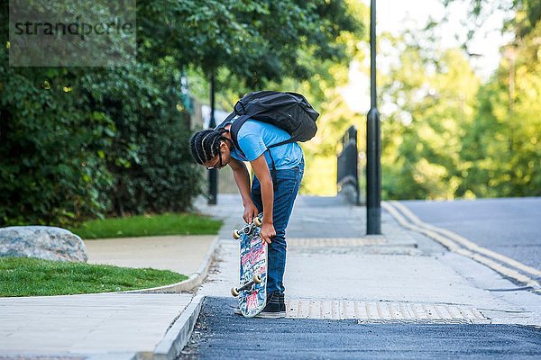 Junge überprüft sein Skateboard auf dem Bürgersteig