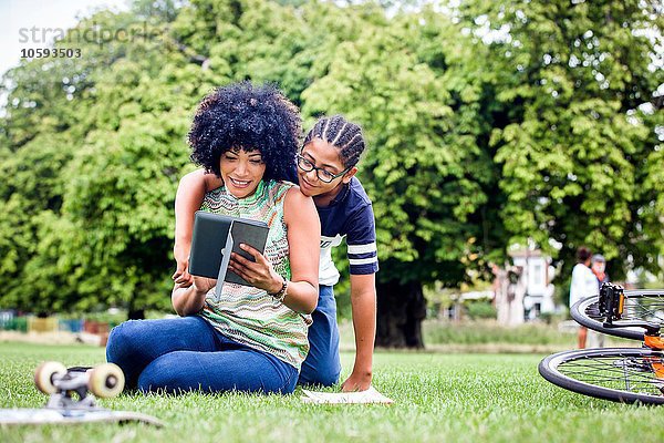 Junge und Mutter lesen gemeinsam digitales Tablett im Park
