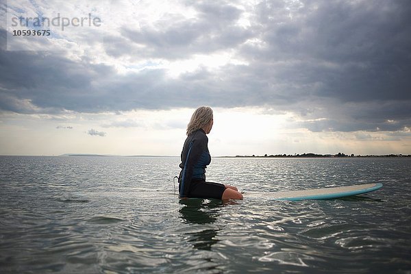 Seniorin auf dem Surfbrett im Meer sitzend  Rückansicht