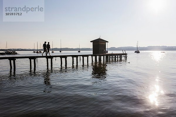 Silhouette des Paares  das auf dem Pier am See zum Bootshaus geht  Schondorf  Ammersee  Bayern  Deutschland