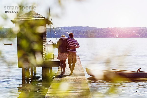 Rückansicht des jungen Paares  das am Pier entlang zum Bootshaus geht  Schondorf  Ammersee  Bayern  Deutschland