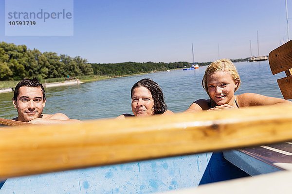 Freunde mit nassen Haaren im See halten sich am Boot und schauen in die Kamera  Schondorf  Ammersee  Bayern  Deutschland