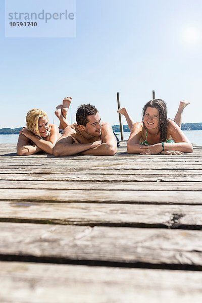 Ebenerdige Ansicht von Freunden  die auf dem Holzsteg liegen  Sonnenbaden  Schondorf  Ammersee  Bayern  Deutschland