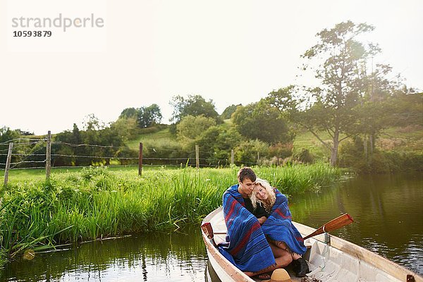 Junges Paar in Decke gewickelt und gekuschelt im Fluss-Ruderboot