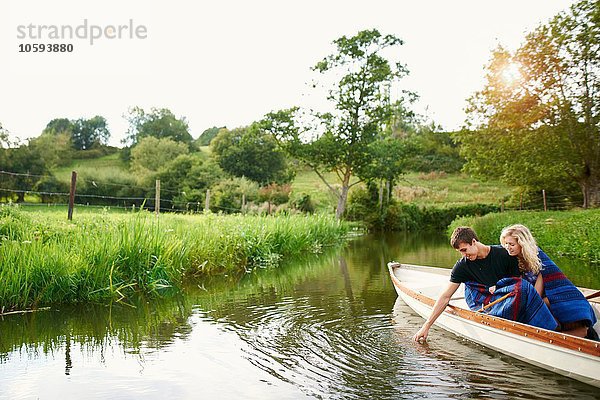 Junger Mann mit Freundin beim Berühren von Wasser aus dem Fluss-Ruderboot