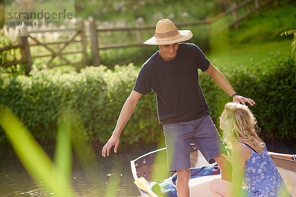 Junger Mann mit Freundin steht im Ruderboot auf dem Fluss