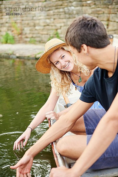 Junges Paar berührt Wasser vom Ruderboot auf dem Landfluss