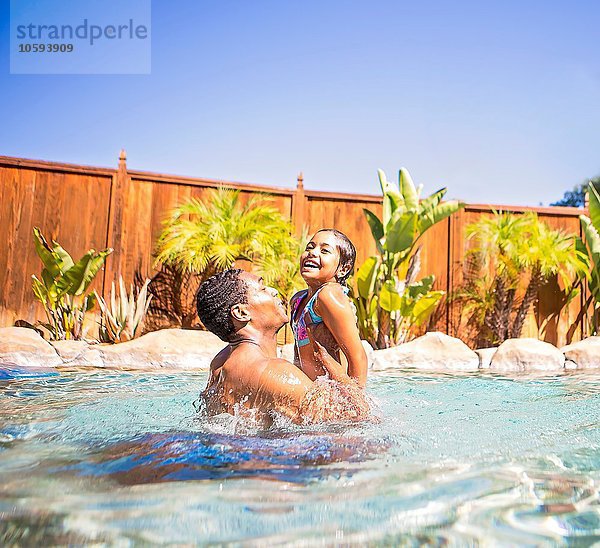 Seitenansicht des Vaters beim Anheben der lächelnden Tochter im Schwimmbad