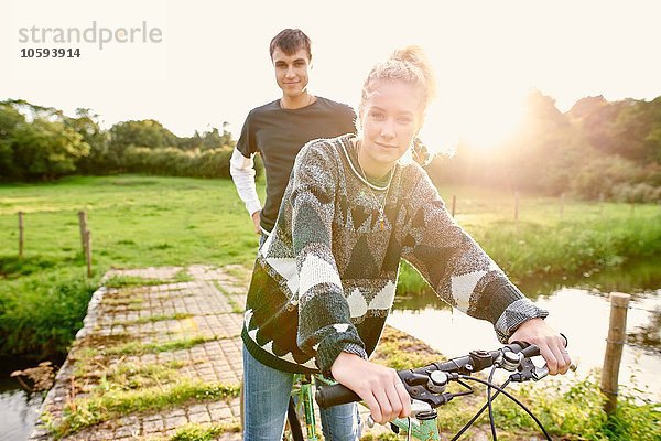 Porträt eines jungen Paares auf dem Fahrrad an der Flussbrücke