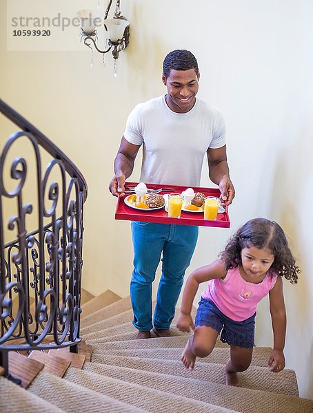 Vater und Tochter gehen die Treppe hinauf und tragen das Frühstück auf dem Tablett.