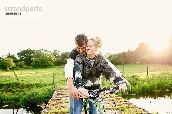 Junges Paar teilt sich das Fahrrad an der Flussbrücke