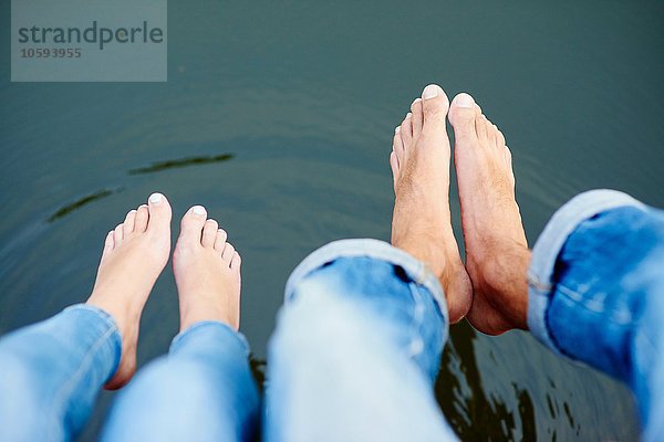 Draufsicht auf die nackten Füße und Beine des jungen Paares auf der Flussbrücke