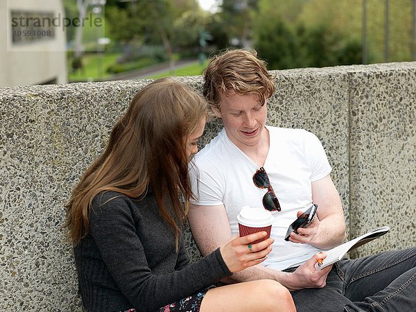 Junges Paar beim Kaffee  mit dem Smartphone  gegen die Betonwand  Melbourne  Victoria  Australien