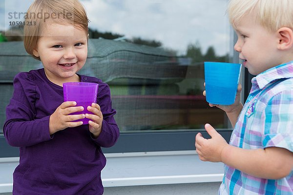 Junge und Kleinkind trinken aus Plastikbechern auf der Terrasse