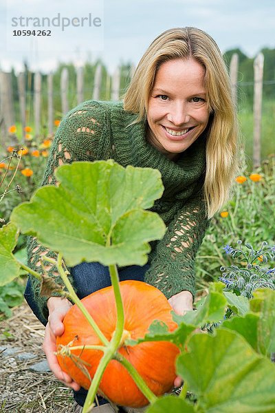 Porträt einer erwachsenen Frau  die Kürbis im Garten pflegt.