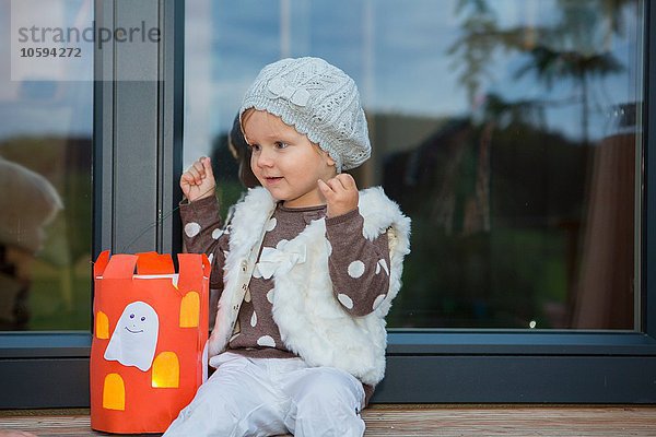 Kleinkind auf Fensterbank sitzend mit hausgemachter Halloween Laterne