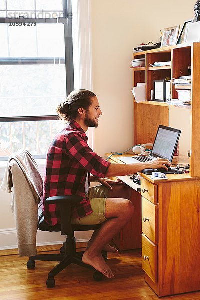 Junger Mann am Schreibtisch sitzend  mit Laptop