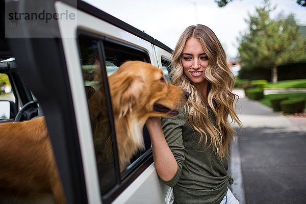 Junge Frau streichelt ihren Hund am Jeepfenster