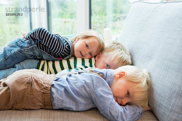 Porträt eines müden Jungen und zweier Kleinkinder  die auf dem Sofa liegen.