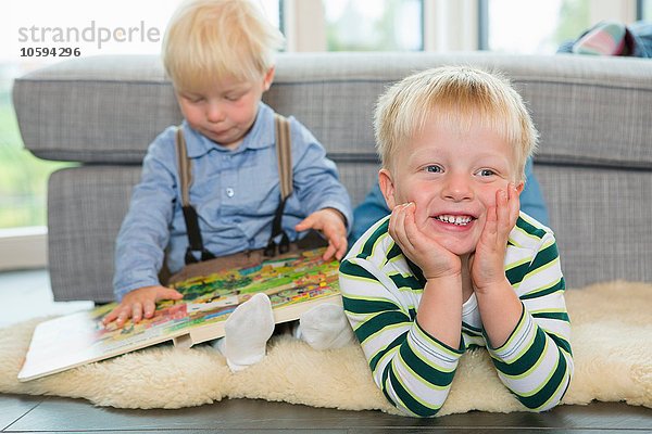 Männliches Kleinkind liest Kinderbuch auf dem Wohnzimmerboden