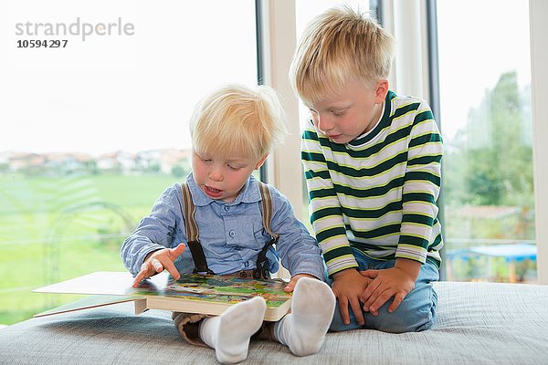 Männliches Kleinkind und Bruder lesen Kinderbuch auf Sofa