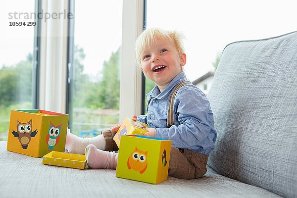 Porträt eines glücklichen männlichen Kleinkindes  das mit Bausteinen auf dem Sofa spielt.