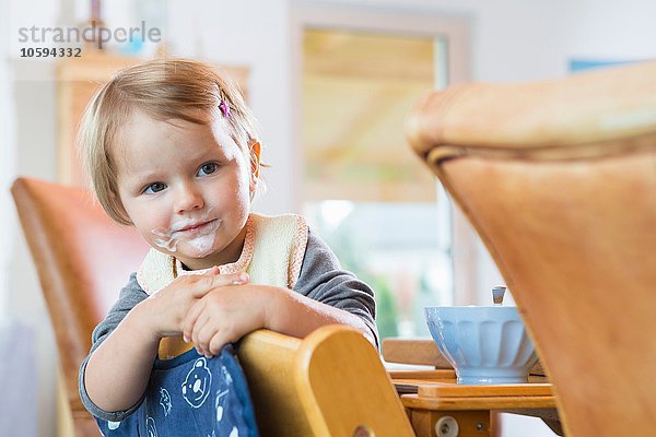 Porträt eines weiblichen Kleinkindes  das sich auf einen Esszimmerstuhl stützt.