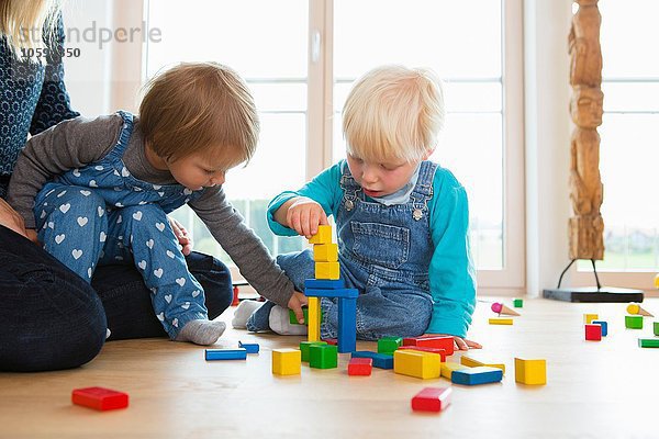 Mittlere erwachsene Frau und zwei Kleinkinder  die mit Bausteinen auf dem Wohnzimmerboden spielen.