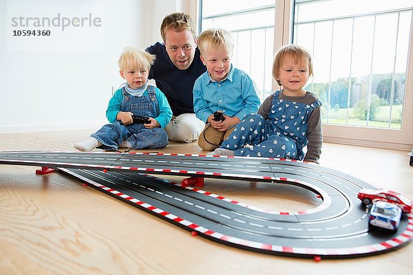 Mittlerer Erwachsener Mann und drei kleine Kinder spielen mit Spielzeug-Rennwagen auf dem Wohnzimmerboden.