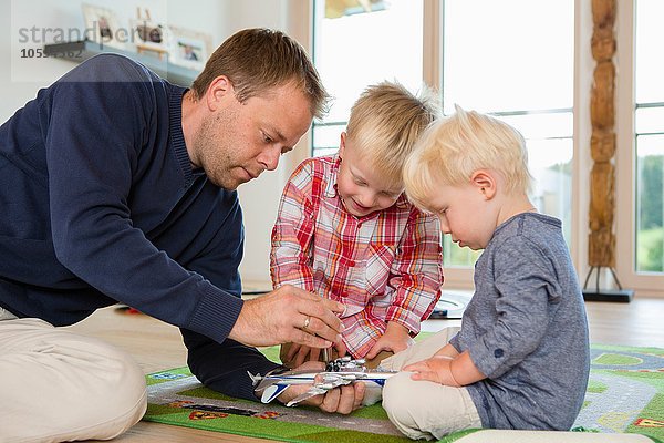 Mittlerer Erwachsener Mann und zwei Söhne bereiten ein Spielzeugflugzeug auf dem Wohnzimmerboden vor.