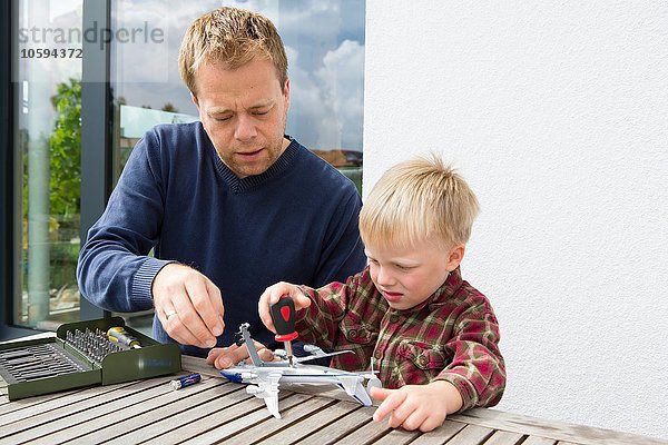 Mittlerer Erwachsener Mann und Sohn bereiten Spielzeugflugzeug auf Terrassentisch vor.