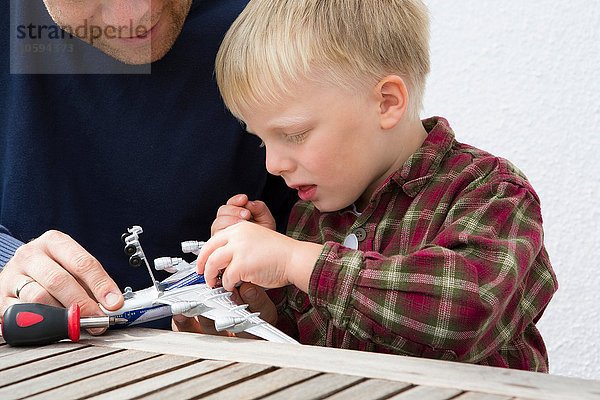 Mittlerer Erwachsener Mann und Sohn bereiten Spielzeugflugzeug auf Terrassentisch vor.