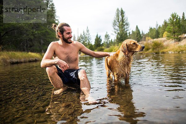 Junger Mann sitzend in River Petting Dog  Lake Tahoe  Nevada  USA