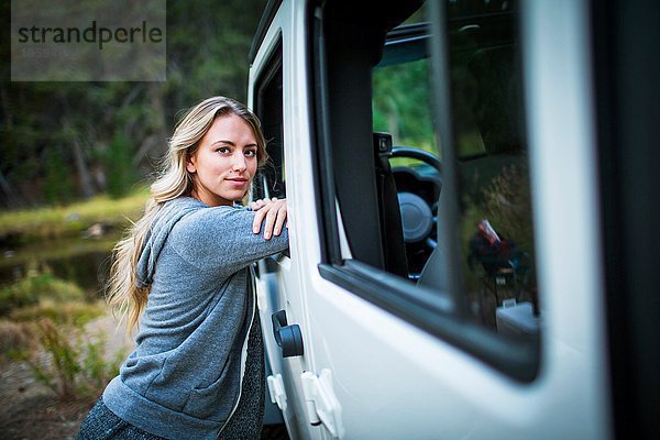 Porträt einer jungen Frau  die sich am Flussufer  Lake Tahoe  Nevada  USA  gegen den Jeep lehnt.