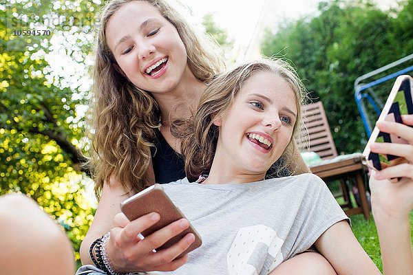 Zwei Teenager-Mädchen beim Lesen von Smartphone-Texten im Garten