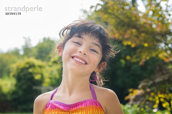 Porträt eines Mädchens mit farbenfrohem Neckholder-Top  das lächelnd auf die Kamera blickt.