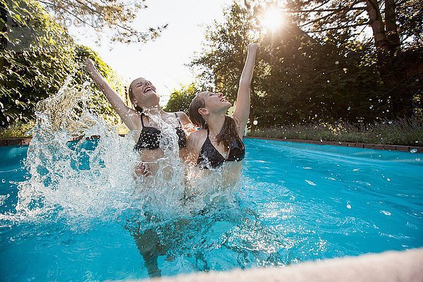 Zwei Teenager-Mädchen springen mit erhobenen Armen im Schwimmbad