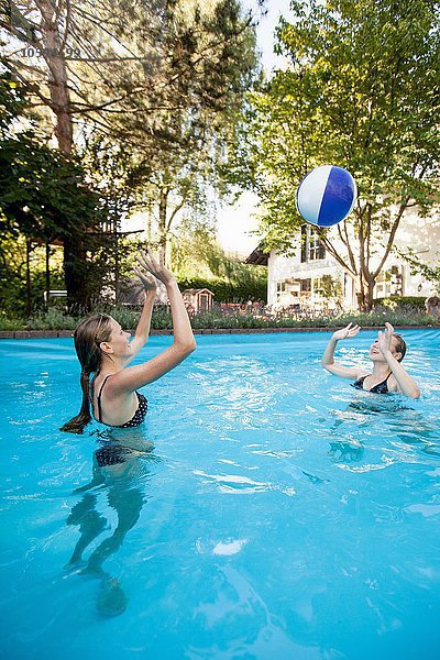 Zwei Teenager-Mädchen spielen mit Beachball im Schwimmbad