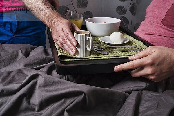 Nahaufnahme eines Mannes  der eine Kaffeetasse auf das Frühstückstablett stellt  um seinen Freund im Bett zu sehen.