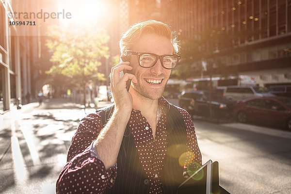 Fröhlicher junger Geschäftsmann beim Spazierengehen auf dem Smartphone  New York  USA