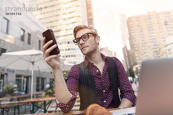 Gestresster junger Geschäftsmann liest Smartphone im Bürgersteigcafé  New York  USA