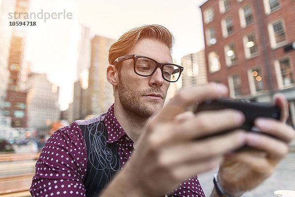 Ernsthafter junger Geschäftsmann liest Smartphone-Text im Bürgersteigcafé  New York  USA