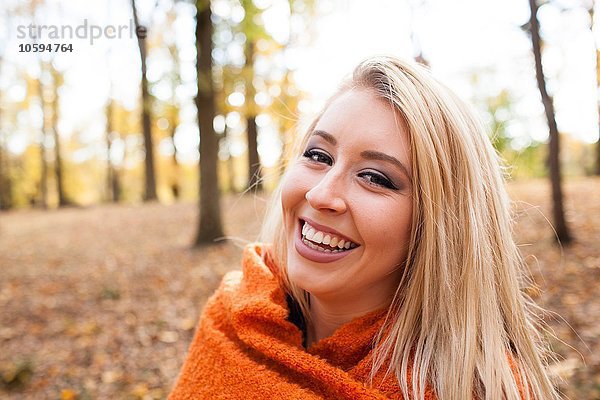Porträt einer jungen Frau mit langen blonden Haaren in Decke gehüllt im Herbstwald